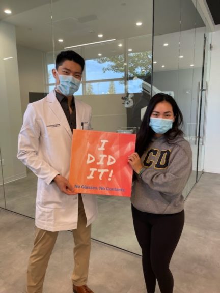 Dr. Joseph Ling & Female patient wearing medical face masks in front of Laser Eye Center of Silicon Valley's laser surgery room holding post-op sign