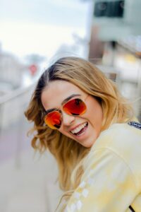 Blonde woman smiling wearing orange sunglasses - What You Need to Know About Sunglasses