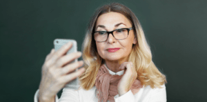 Older woman wearing glasses holding up and iPhone for How Monovision LASIK Can Correct Near Vision blog
